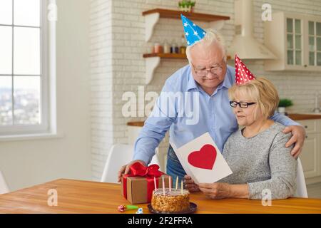 Der ältere Ehemann gratulierte seiner Frau zu ihrem Geburtstag, gab ihr Kuchen, Geschenk und Grußkarte Stockfoto