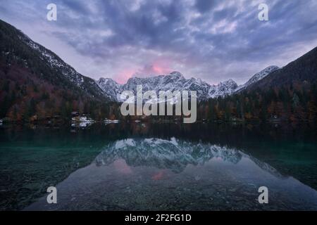 Sonnenuntergang über dem Lower Fusine Lake während der Laubsaison mit Schnee Spitzen im Hintergrund und eine schöne Reflaktion im Kristallklares Wasser Stockfoto