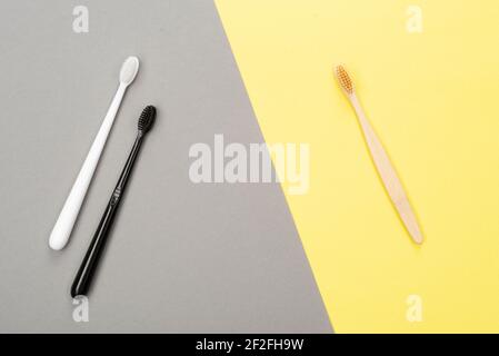 Eine ökologische Zahnbürste aus natürlichem Bambus und zwei Kunststoff-Zahnbürsten liegen auf einem gelb-grauen Hintergrund. Draufsicht, flach liegend. Sustainabl Stockfoto