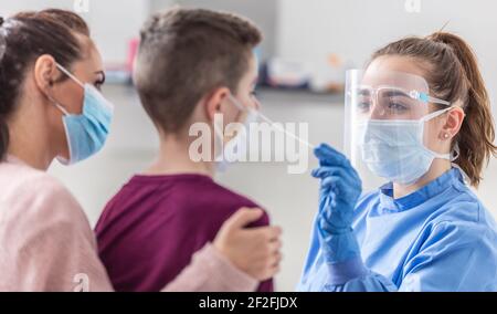 Mama hält ihren Sohn, während medizinische Arbeiter Probe aus seiner Nase während Coronavirus Pandemie-Tests nimmt. Stockfoto