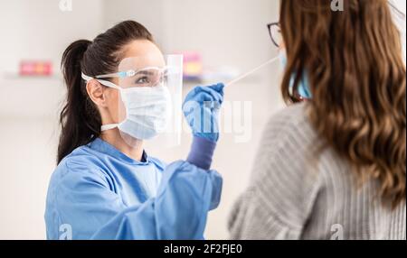 Eine medizinische Mitarbeiterin mit Schutzausrüstung nimmt die Probe von der Nase eines Patienten zum Antigentest auf Coronavirus. Stockfoto