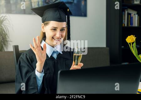 Soziale Distanzierung Graduierung Partei - weibliche Absolvent trägt Kleid und Feiern Sie Bachelor-Abschluss online mit College-Freunden zu Hause Stockfoto