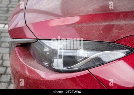 headlight of a red dirty car side view on parts of the car in a layer of dry dust close-up, nobody. Stockfoto
