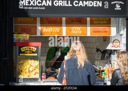 London, Großbritannien - 26. Februar 2021 - EIN männliches Personal, das eine Gesichtsmaske trägt und Kunden am mexikanischen Imbissstand in Camden Market bedient Stockfoto