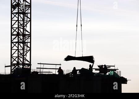 Silhouetten von Arbeitern und Kran auf der Baustelle gegen den Himmel. Wohnungsbau, Bauherren arbeiten auf Gerüsten Stockfoto