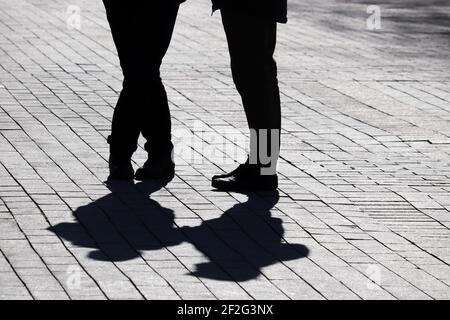 Silhouetten und Schatten eines Paares auf der Straße, zwei Menschen, die auf dem Fußgängerweg stehen. Konzept der Beziehungen, Stadtleben, dramatische Geschichten Stockfoto
