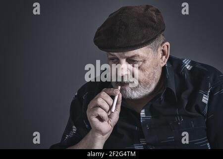 Dramatische Low-Key-Porträt des zögernden kaukasischen älteren Mann mit Zigarette Stockfoto