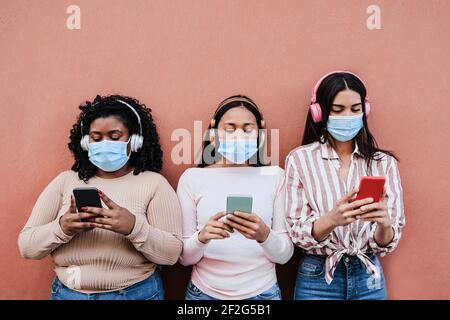 Junge, multirassische Menschen tragen Sicherheitsmasken, während sie Mobiltelefone benutzen Outdoor - Hauptfokus auf Mitte Mädchen Stockfoto