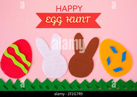 Ausschneiden von Filzanwendungen von Eiern und weißen und braunen Kaninchen auf dem Gras. Rosa Hintergrund. Flach liegend. Osterferien. Stockfoto