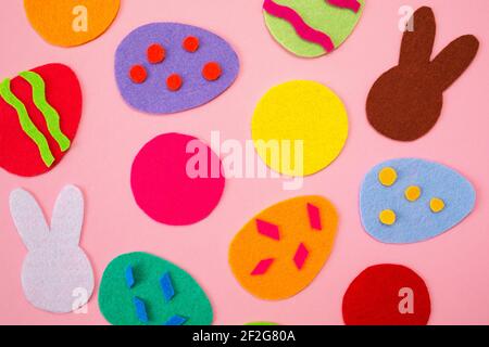 Abstraktes Bild von ausgeschnittenen Filzapplikationen von bunten Eiern und weißen und braunen Kaninchen. Rosa Hintergrund. Flach liegend. Osterferien. Stockfoto