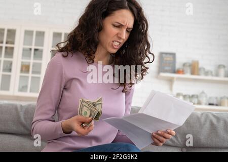 Trauriges junges Mädchen, das letztes Bargeld hält, das Gefühl der Angst über Schuld oder Bankrott, zu Hause sitzend. Stockfoto