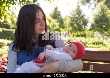 Die junge Mutter hält ein neugeborenes Baby in den Armen für einen Spaziergang im Park. Selektiver Fokus. Stockfoto