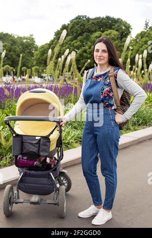 Junge Mutter im Park auf einem Spaziergang mit einem kleinen Kind im Kinderwagen. Selektiver Fokus. Stockfoto