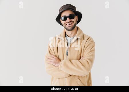 Porträt eines glücklichen jungen Mannes in beigefarbener Jacke, Mütze und Sonnenbrille auf isoliertem weißem Hintergrund Stockfoto