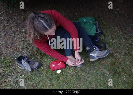 Frau behandelt Blister auf dem Fuß während einer Wanderung, Bergwanderung, erste Hilfe, Notfall Stockfoto