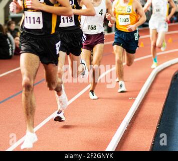 Eine Reihe von Läufern auf einer Indoor-Strecke, die bei einem Wettkampfrennen die Meile rast. Stockfoto