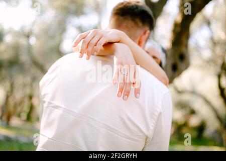 Die Braut umarmt den Bräutigam sanft im Park und wickelt ihre Arme aus nächster Nähe um seinen Hals Stockfoto