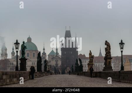 Prag, Tschechische Republik - 24. Februar 2021.Blick auf die Karlsbrücke, Altstädter Brückenturm in kalten nebligen Morgen. Menschen, die durch die Stadt gehen. Stockfoto