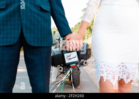 Hochzeit, frisch vermählt. Ein Mann und Frauen in Hochzeitskleider halten sich die Hände. Im Hintergrund ist ein Motorrad dazwischen. Nahaufnahme der Hände Stockfoto