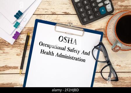 Papier mit Text OSHA - Occupational Safety and Health Administration auf dem Bürotisch, Rechner und Tasse Kaffee Stockfoto