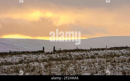 Sonnenuntergang über den schneebedeckten Hügeln, Feldern und Trockensteinmauern von Weardale, The North Pennines, County Durham, Großbritannien Stockfoto