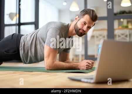 Schöner junger Mann mit Laptop und dabei Plank Stockfoto