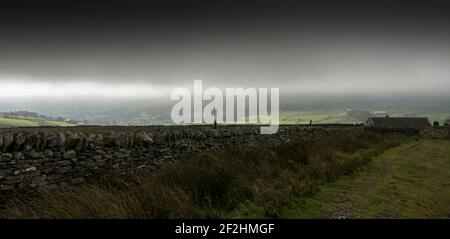 Eine unwirtliche Landschaft aus Trockensteinmauer, Bauernhaus und dunkelgrauem Himmel in den North Pennines, Weardale, County Durham, Großbritannien. Stockfoto