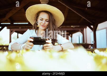 Lächelnde trendige Frau in weißem Hemd mit Hut senden Textnachricht per Smartphone auf der Ranch. Stockfoto
