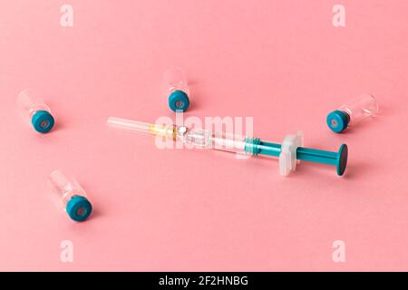 Spritze mit mehreren medizinischen Fläschchen zur Injektion auf rosa Hintergrund. Stockfoto