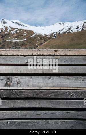Verblasste, graue Holzzaun vor der schneebedeckten Hügelkette bei San Bernardino, Schweiz Stockfoto