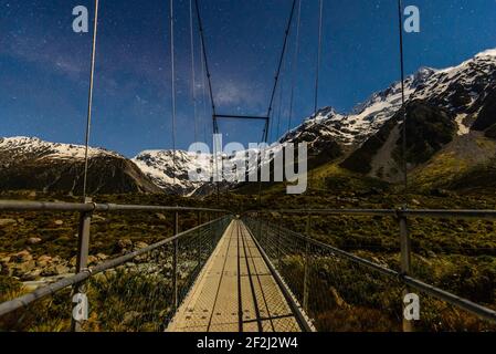 Wanderblick beim Wandern auf der langen Brücke auf dem Hooker Mountain Track, Neuseeland. Schneebedeckte Berge unter Sternen am Himmel. Stockfoto