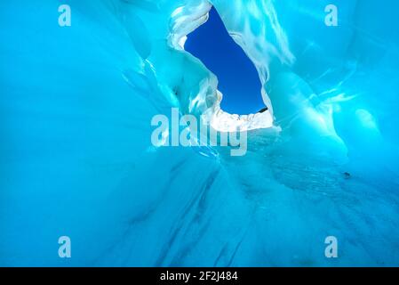 Weg durch den Eistunnel im Fox Glacier, South Island, Neuseeland. Sonnenstrahlen, die auf der Oberfläche scheinen, erzeugen einen erstaunlichen blauen Eishöhleneffekt. Stockfoto