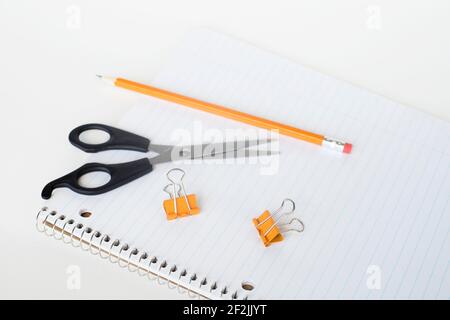 Notizblock, Binderclips, Schere und Bleistift. Gestreiftes, rohles Notizbuch mit Papeterie auf weißem Hintergrund. Stockfoto