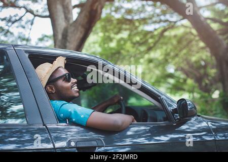Glücklicher afrikanischer Fahrer lächelt, während er in einem Auto mit sitzt Öffnen Sie die Frontscheibe Stockfoto