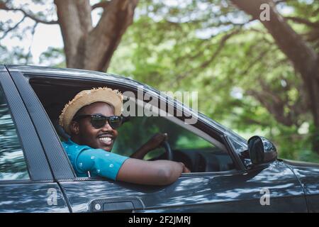 Glücklicher afrikanischer Fahrer lächelt, während er in einem Auto mit sitzt Öffnen Sie die Frontscheibe Stockfoto