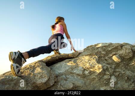 Frau Wanderer Klettern steilen großen Felsen an einem sonnigen Tag. Junge Kletterin überwindet schwierige Kletterrouten. Aktive Erholung in der Natur Konzept. Stockfoto