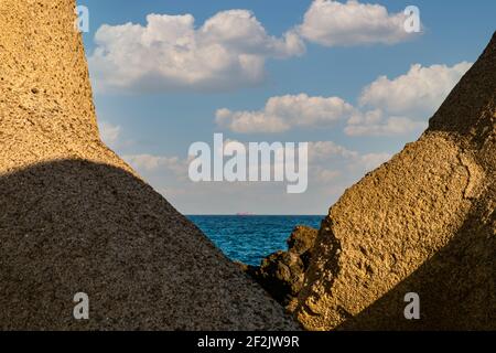 Vulkanische Felsen, dunkelblaues Meer und Frachtschiff am Horizont. Stockfoto