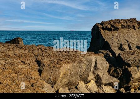 Vulkanische Felsen, dunkelblaues Meer und Frachtschiff am Horizont. Stockfoto