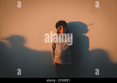 Boy steht gegen eine Wand mit seinem Schatten während des Sonnenuntergangs Stockfoto