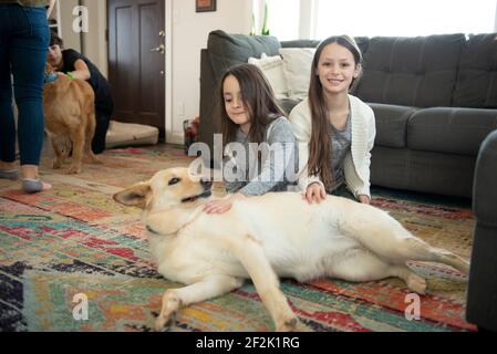 Zwei Mädchen spielen mit einem Hund im Wohnzimmer. Stockfoto