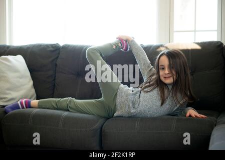 Kleines Mädchen goofing herum auf der Couch durch ein Fenster. Stockfoto