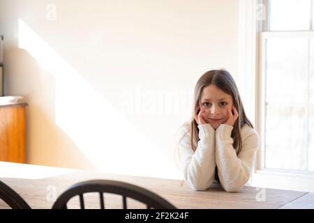 Schönes Mädchen, das an einem Bauerntisch in der Sonne sitzt. Stockfoto
