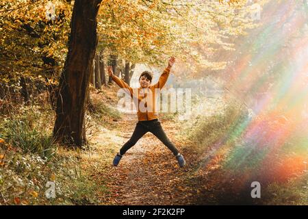 Junge springt in die Luft auf Pfad unter Baum mit regenbogenlicht Stockfoto