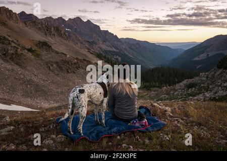 Frau, die Berge beim Wandern mit Hund während des Sonnenuntergangs betrachtet Stockfoto