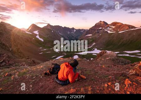 Weibliche Wanderin, die während des Sonnenuntergangs auf dem Berg gegen den Himmel sitzt Stockfoto