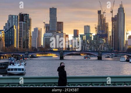 Fußgänger trägt Gesichtsmaske auf Westminster Bridge mit Blick auf die Stadt bei Sonnenuntergang im Hintergrund, London, Dezember 2020 Stockfoto