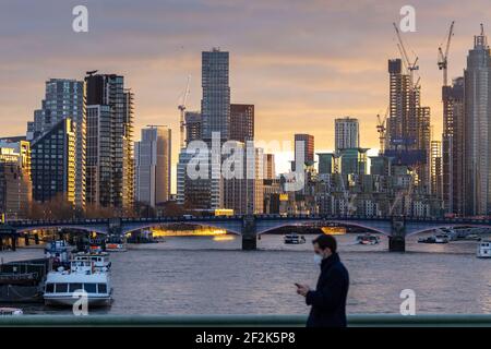 Fußgänger trägt Gesichtsmaske auf Westminster Bridge mit Blick auf die Stadt bei Sonnenuntergang im Hintergrund, London, Dezember 2020 Stockfoto