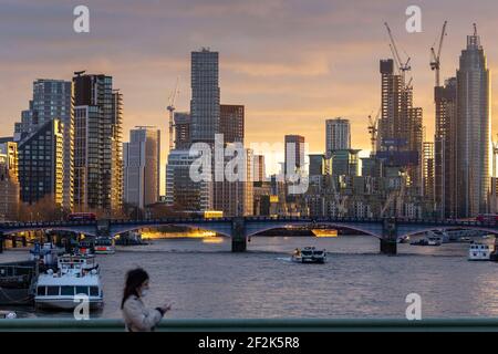 Fußgänger trägt Gesichtsmaske auf Westminster Bridge mit Blick auf die Stadt bei Sonnenuntergang im Hintergrund, London, Dezember 2020 Stockfoto