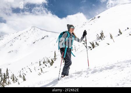 Lächelnde junge Frau mit Rucksack Häutung auf schneebedeckten Berg während Urlaub Stockfoto