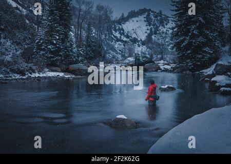 Frau Fliegenfischen im Fluss während Schneefall Stockfoto